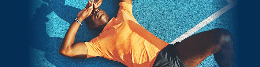 Person lying on a blue track surface wearing an orange shirt