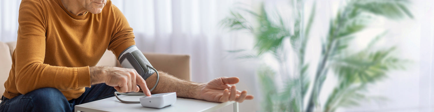 Person measuring blood pressure at home with a device on a table.